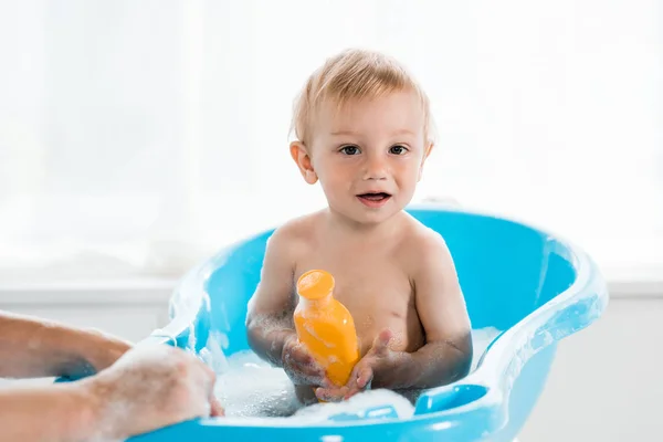 Cropped view of mother near happy toddler kid holding bottle with shampoo — Stock Photo