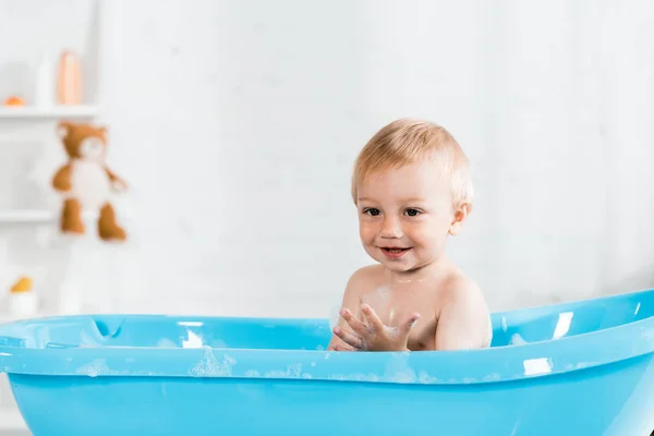 Cute toddler kid smiling while taking bath in blue baby bathtub — Stock Photo