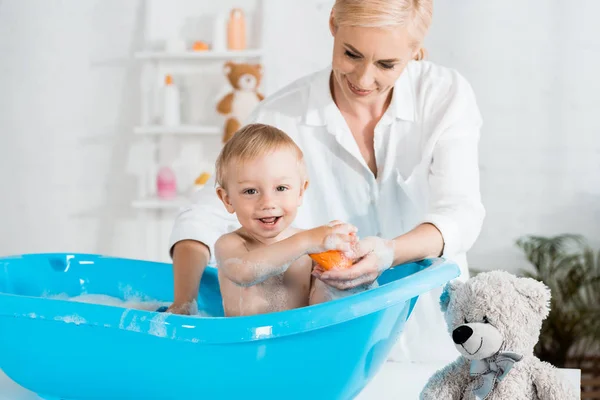 Happy toddler kid smiling near mother while taking bath at home — Stock Photo