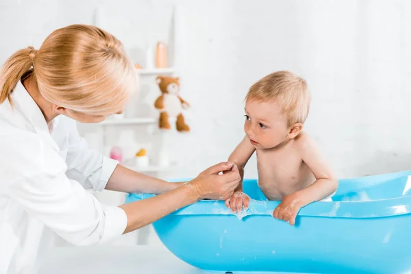 Blonde Mutter in der Nähe entzückender Kleinkind-Sohn badet im Badezimmer — Stockfoto