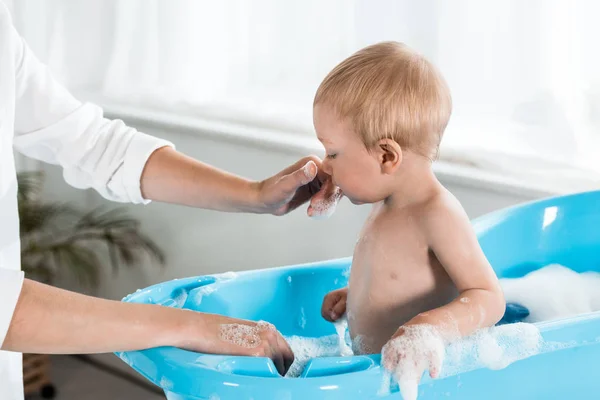 Vista recortada de la madre tocando la nariz de lindo hijo pequeño en el baño - foto de stock