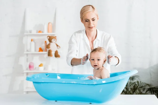 Rubia madre lavado cabeza de lindo niño hijo en cuarto de baño - foto de stock