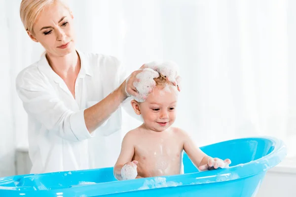 Attractive blonde mother washing head of cute toddler son in bathroom — Stock Photo