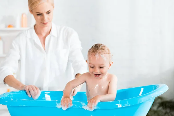 Вибірковий фокус веселого малюка, який посміхається у ванній біля матері — стокове фото