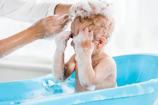 Ausgeschnittene Ansicht der Mutter, die den Kopf ihres Kleinkindes im Badezimmer wäscht — Stockfoto