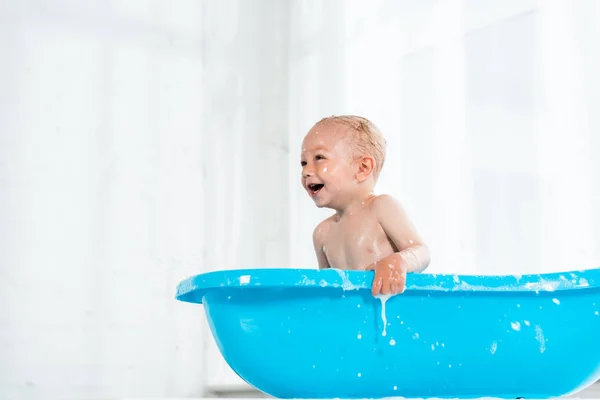 Low angle view of cute toddler kid smiling in plastic baby bathtub — Stock Photo