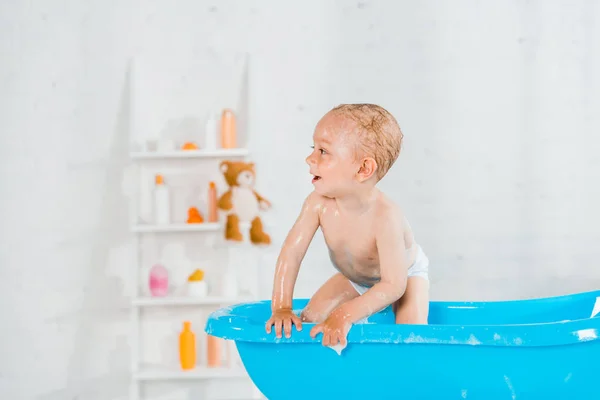 Naked and cute toddler kid smiling in plastic baby bathtub — Stock Photo
