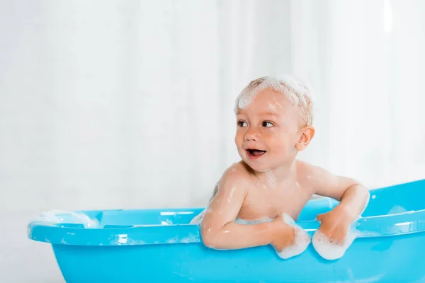 Niño pequeño desnudo y lindo sonriendo mientras toma el baño en bañera de plástico del bebé - foto de stock