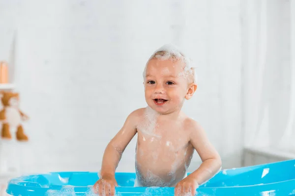Adorable toddler kid taking bath and smiling in blue plastic baby bathtub — Stock Photo