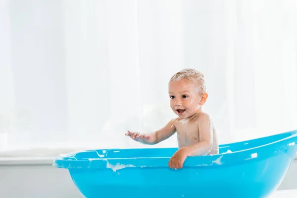 Adorable toddler child taking bath and smiling in blue plastic baby bathtub — Stock Photo