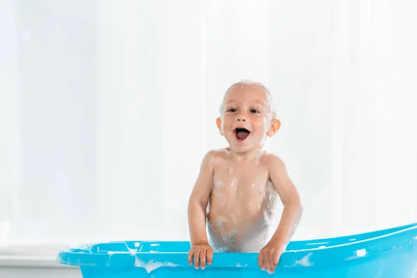 Toddler kid taking bath and smiling in blue plastic baby bathtub — Stock Photo