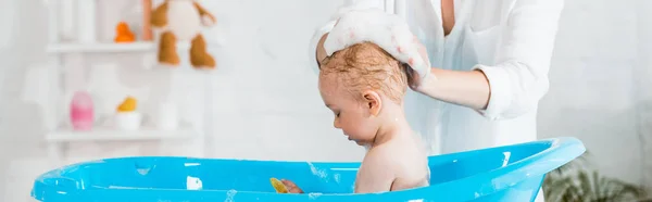 Panoramic shot of  mother washing head of cute toddler son in bathroom — Stock Photo