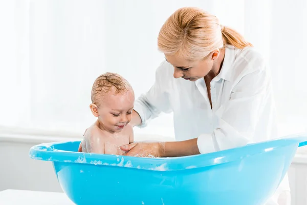 Attrayant blonde mère lavage tout-petit fils dans la salle de bain — Photo de stock