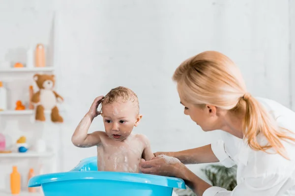 Приваблива блондинка мати дивиться на мокрий маленький син у ванній кімнаті — стокове фото