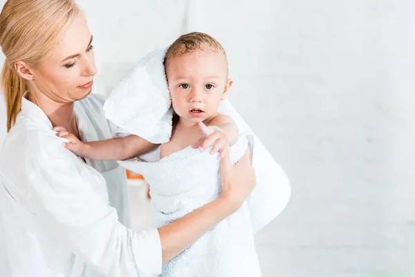 Attractive blonde mother holding in arms adorable toddler son in bathroom — Stock Photo