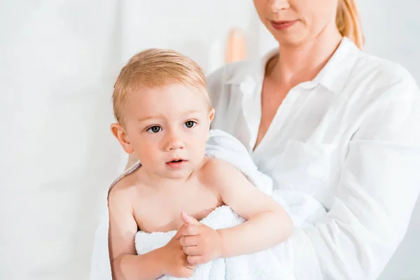 Vue recadrée de mère blonde tenant dans les bras mignon tout-petit fils dans la salle de bain — Photo de stock