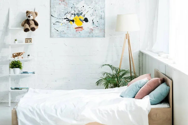 Bett mit weißer Bettwäsche, blauen und rosa Kissen in der Nähe von Gestell und Malerei — Stockfoto