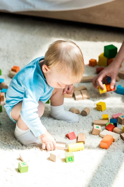 Vista ritagliata della donna vicino al figlio del bambino che gioca con mattoni da costruzione sul tappeto a casa — Foto stock