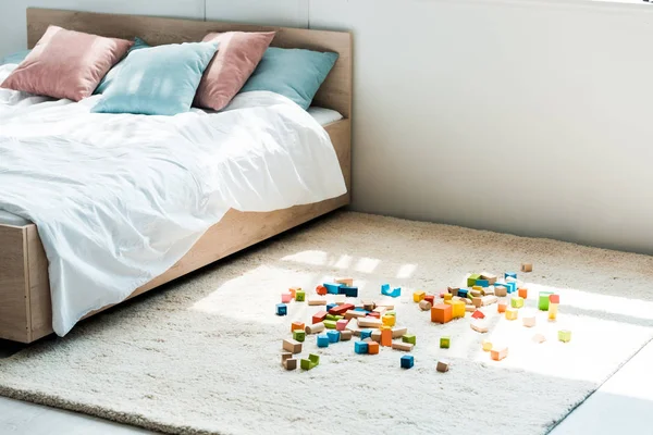 Blocs jouets près du lit avec literie blanche, oreillers bleu et rose — Photo de stock