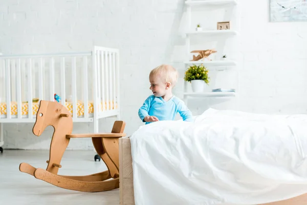 Glückliches Kleinkind steht neben hölzernem Schaukelpferd im modernen Schlafzimmer — Stockfoto