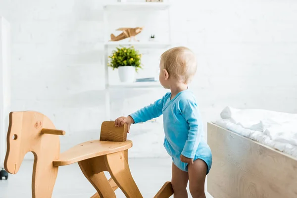 Kleinkind steht neben Schaukelpferd im modernen Schlafzimmer — Stockfoto