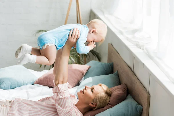 Feliz madre sosteniendo en brazos lindo niño hijo mientras está acostado en la cama - foto de stock