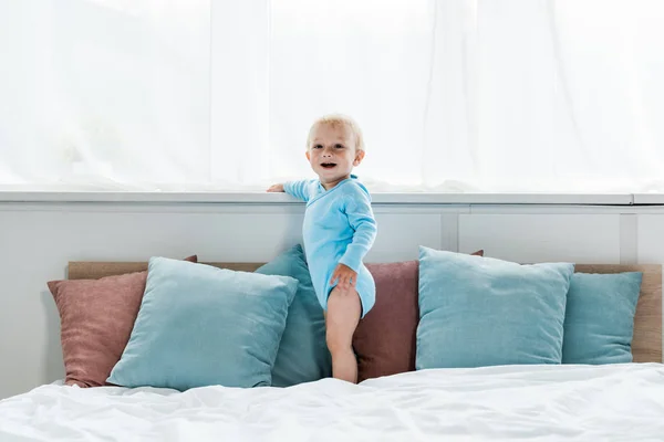 Niño feliz niño de pie en la cama y sonriendo en el dormitorio - foto de stock