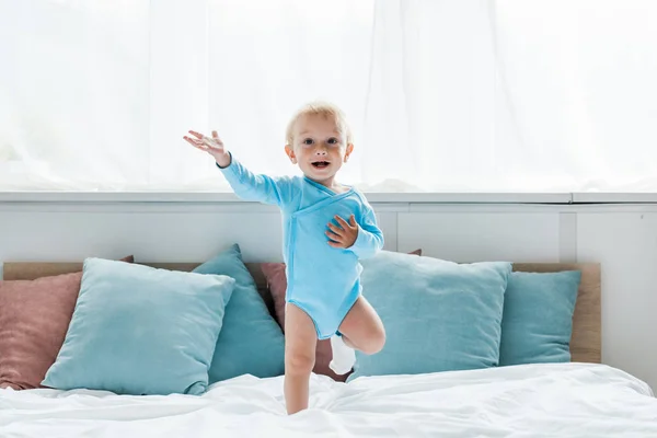 Cheerful kid gesturing while jumping on bed in modern bedroom — Stock Photo