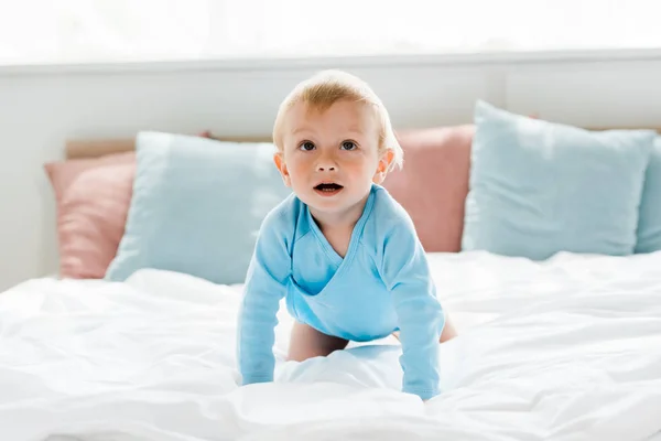 Niedliche Kleinkind krabbeln auf Bett mit weißen Bettwäsche und Kissen zu Hause — Stockfoto