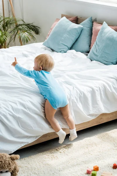 Bambino che striscia sul letto con biancheria da letto bianca e punta con il dito a casa — Foto stock