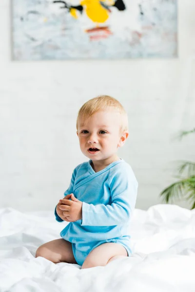 Cute toddler boy sitting on bed with white bedding at home — Stock Photo