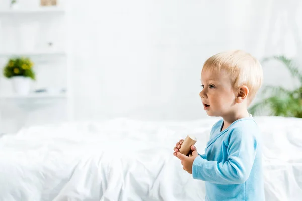 Bonito criança de pé com brinquedo de madeira perto da cama — Fotografia de Stock