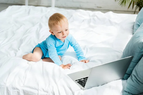 Happy toddler kid looking at laptop while sitting on bed at home — Stock Photo