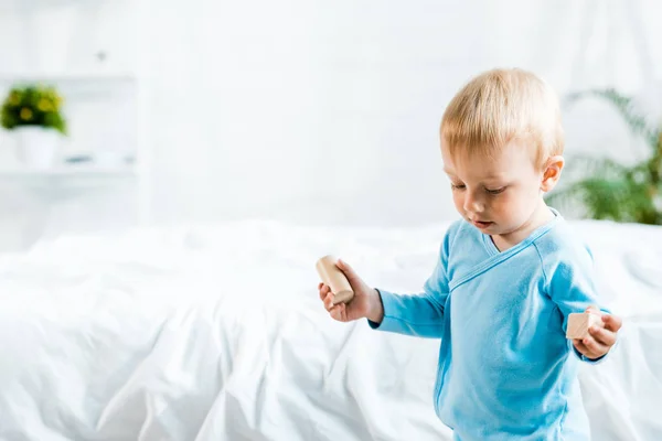 Adorável criança de pé com brinquedos de madeira perto da cama em casa — Fotografia de Stock