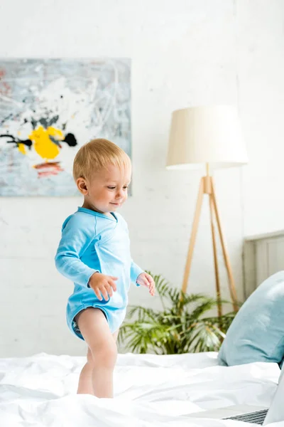 Happy adorable toddler kid standing on bed near laptop — Stock Photo