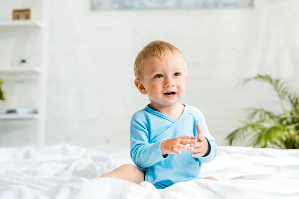 Adorabile bambino seduto sul letto con lenzuola bianche e gesti a casa — Foto stock