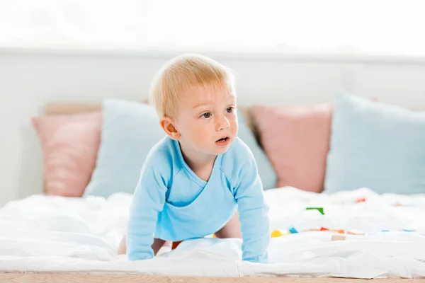 Überraschtes Kleinkind krabbelt mit weißer Bettwäsche zu Hause auf Bett — Stockfoto