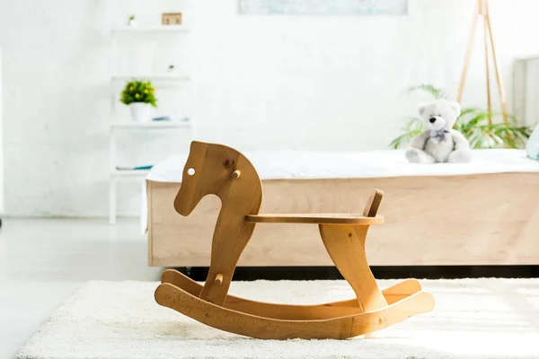 Selective focus of wooden rocking horse near bed with white bedding and teddy bear — Stock Photo