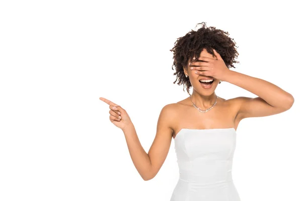 Fröhliche afrikanisch-amerikanische Frau zeigt mit dem Finger, während sie die Augen isoliert auf weiß bedeckt — Stockfoto