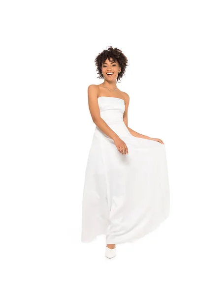 Happy african american bride smiling while touching wedding dress isolated on white — Stock Photo