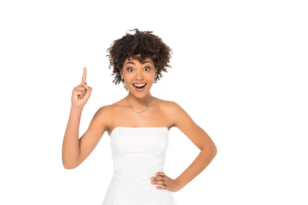 Alegre afroamericana novia mostrando idea signo y de pie con la mano en la cadera aislado en blanco - foto de stock