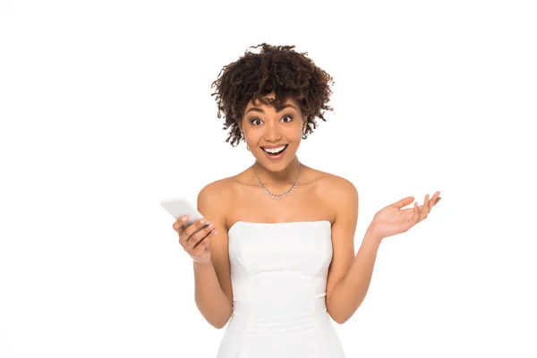 Счастливая африканская американская невеста показывает пожимая плечами жест, держа смартфон изолирован на белом — стоковое фото