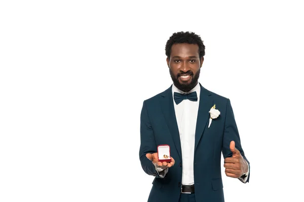 Alegre afroamericano hombre celebración caja con anillo de bodas y mostrando el pulgar hacia arriba aislado en blanco - foto de stock