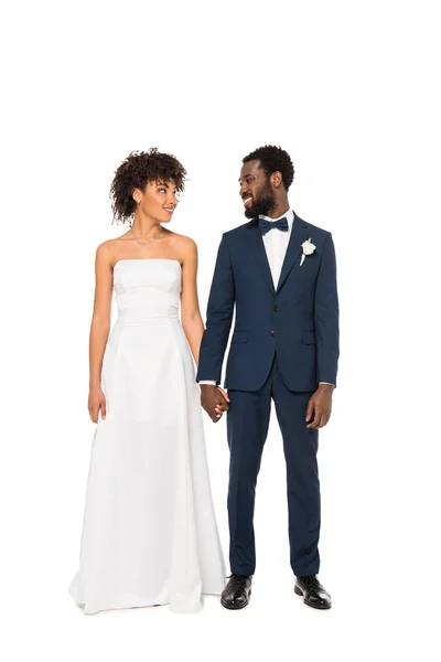 Alegre noiva afro-americana e noivo de mãos dadas enquanto em pé isolado no branco — Fotografia de Stock