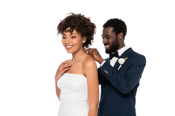 Happy african american bridegroom wearing necklace on attractive bride isolated on white — Stock Photo