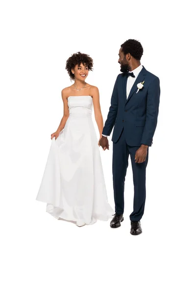 Heureux marié afro-américain tenant la main avec belle mariée en robe de mariée isolé sur blanc — Photo de stock
