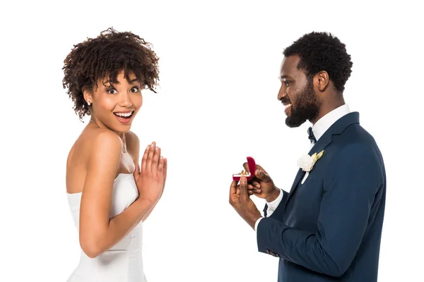 Allegro uomo africano americano che tiene la scatola con anello mentre fa la proposta di donna sorpresa isolata su bianco — Foto stock