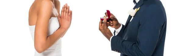 Plano panorámico del hombre afroamericano que sostiene la caja con el anillo mientras que hace la propuesta a la mujer aislada en blanco - foto de stock