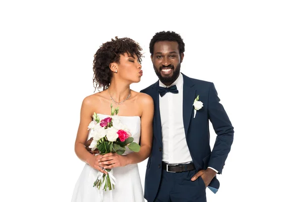 Felice sposa afroamericana con viso d'anatra tenendo bouquet vicino allo sposo con mano in tasca isolato su bianco — Foto stock