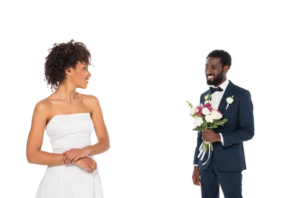 Foco seletivo de noivo barbudo segurando flores perto de noiva americana africana feliz isolado no branco — Fotografia de Stock